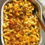 Close-up of baked spicy mac and cheese topped with golden breadcrumbs and melted cheddar in a white casserole dish with a serving spoon.